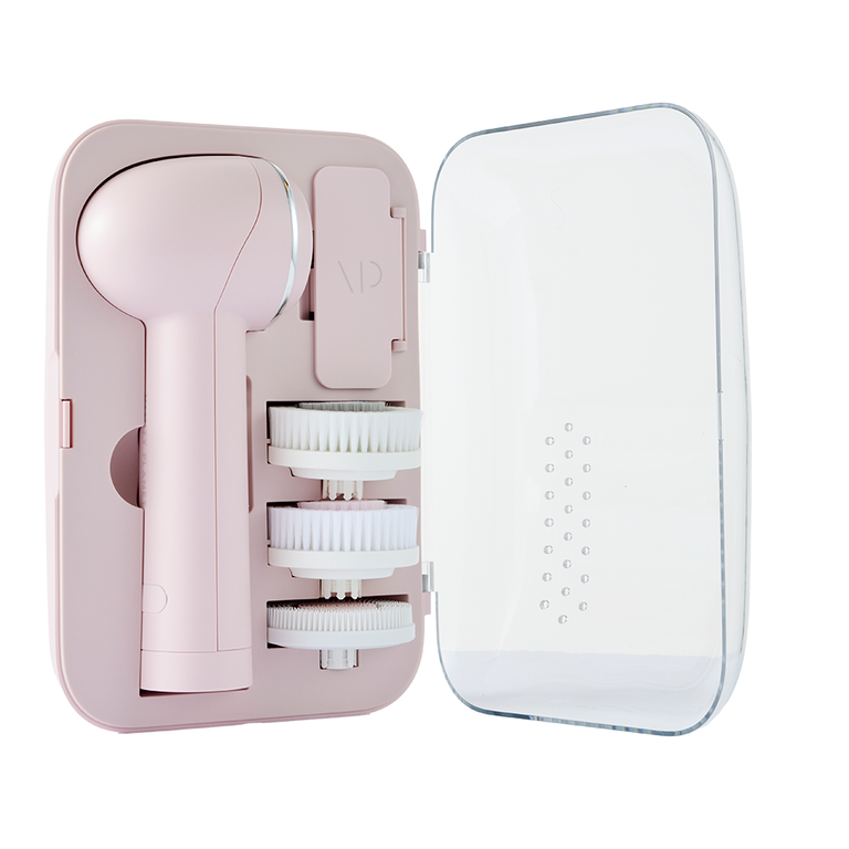 A pink facial cleansing device from Vanity Planet with three white brush attachments stored in a sleek case with a clear cover. The device and brushes are neatly organized in dedicated compartments.
